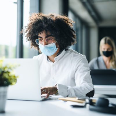man with face mask back at work in office after lockdown, working.